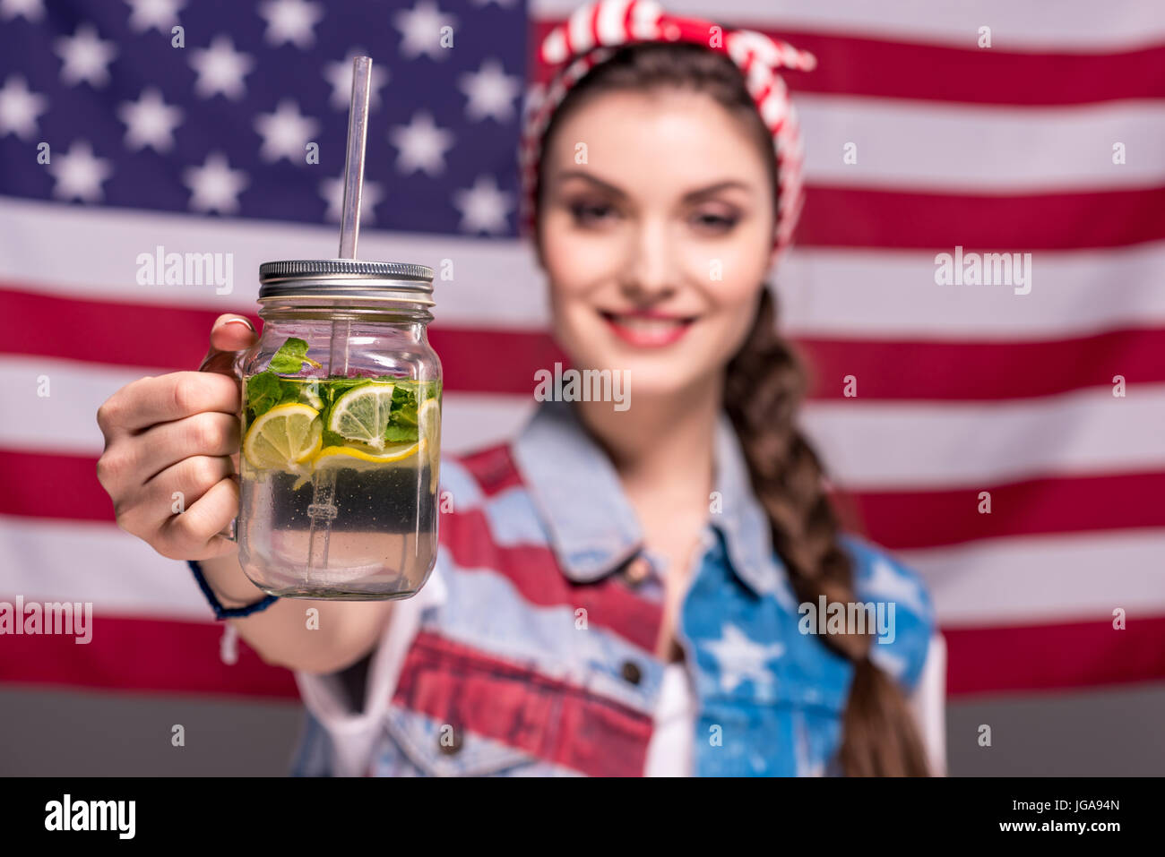 Ritratto di donna sorridente che mostra detox drink in mano con bandiera americana sullo sfondo Foto Stock