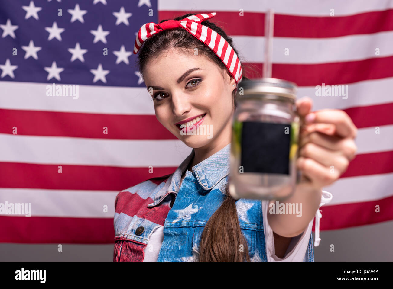 Ritratto di donna sorridente che mostra detox drink in mano con bandiera americana sullo sfondo Foto Stock