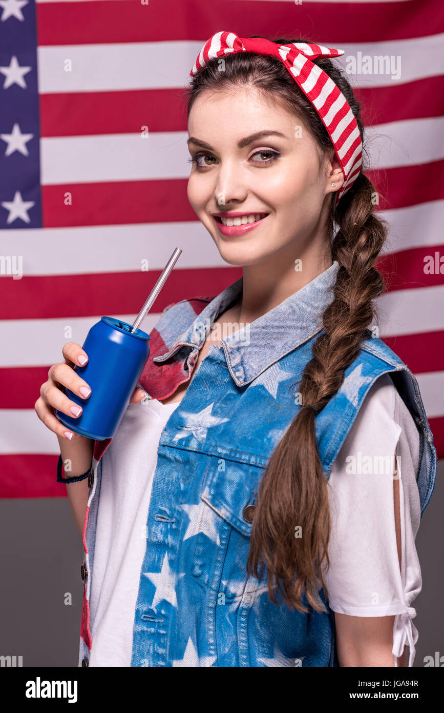 Ritratto di donna sorridente holding drink in mano con bandiera americana dietro Foto Stock