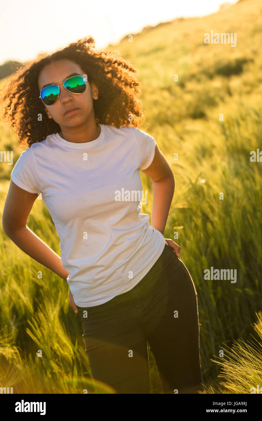 Bellissima gara di misto americano africano ragazza adolescente giovane donna indossa relective aviator occhiali da sole, jeans e una t-shirt bianco in un cornfield Foto Stock