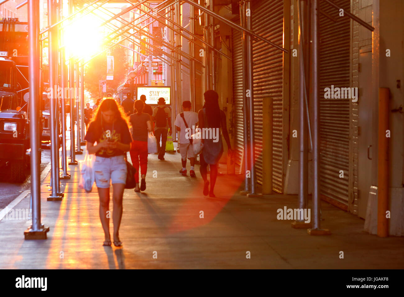 Una persona che cammina verso il basso di una New York City street in una calda giornata estiva con il fumoso nel sole pomeridiano profila bassa e grande in background. Foto Stock