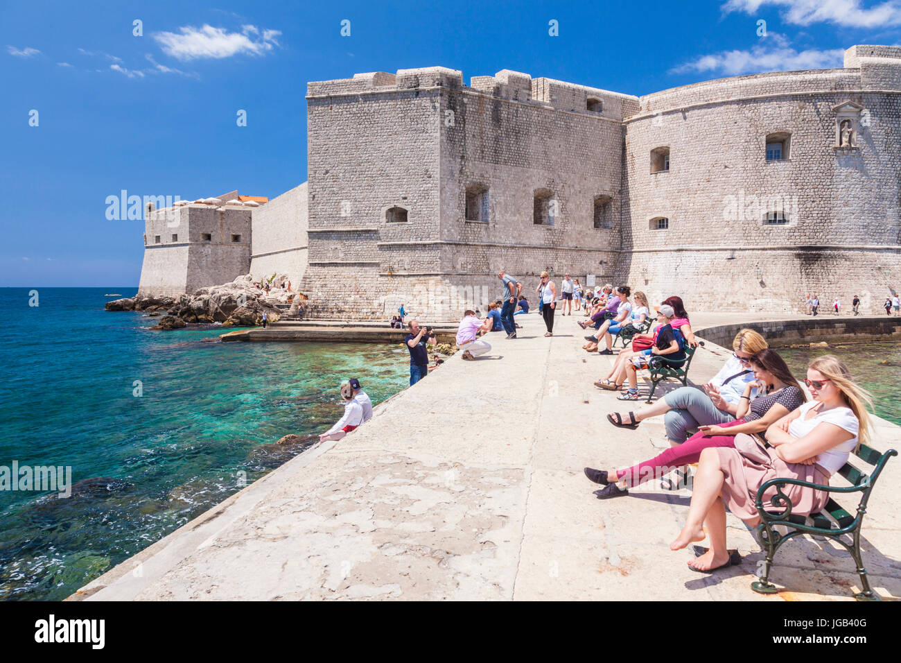Croazia Dubrovnik Croazia costa dalmata turisti seduti sulla parete del mare Arsenal St John Fort dubrovnik porto vecchio le mura della città vecchia di Dubrovnik Foto Stock