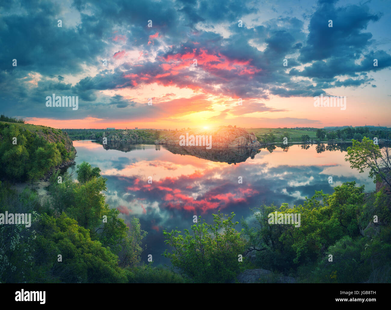 Scena spettacolare con il fiume, verdi alberi, rocce e incredibile cielo blu con nuvole colorate riflettono in acqua al tramonto. Fantastico paesaggio estivo con l Foto Stock