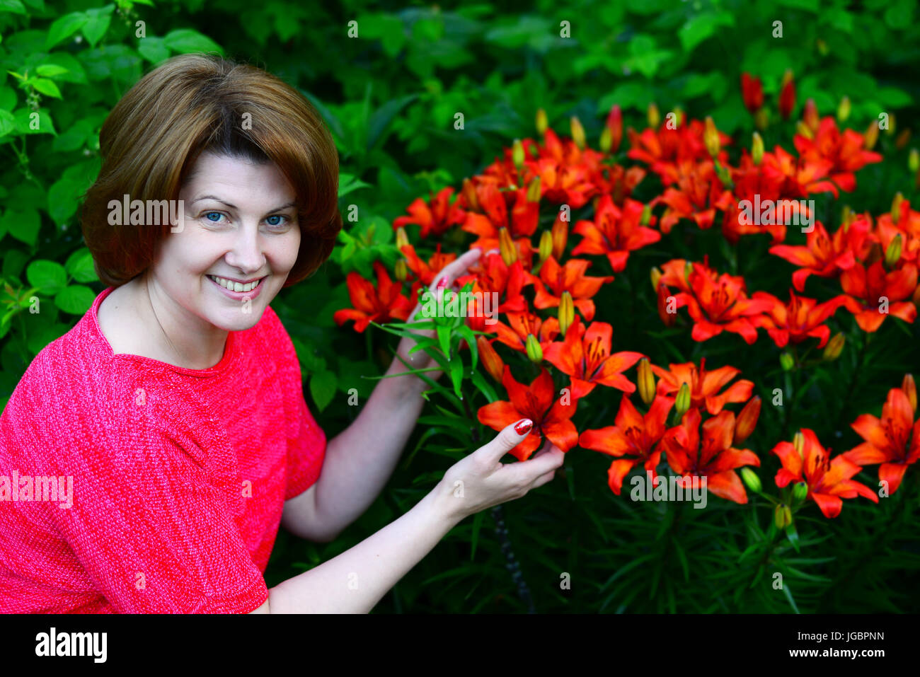 Donna vicino al letto di fiori con gigli arancione Foto Stock