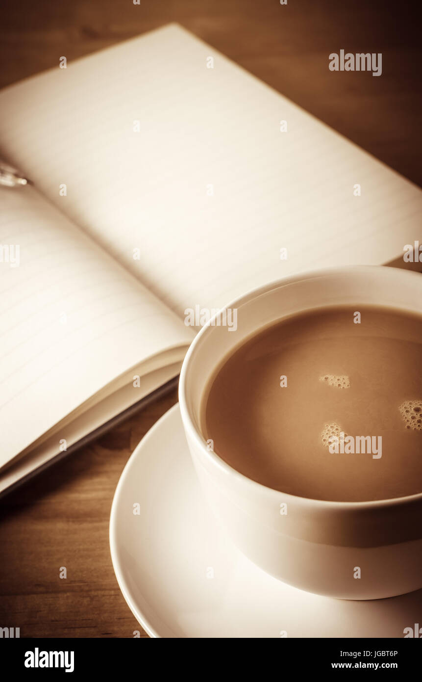 Una tazza di tè in primo piano con apertura ufficiale nel più morbido rivelando di sfondo vuoto pagine rivestito e penna appoggiata sulla parte superiore. Tavolo in legno al di sotto. Foto Stock