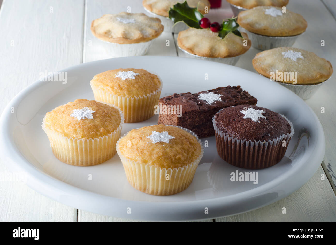 Una selezione di singoli piastrate dolci di Natale e pasticci di carne macinata in fogli piatti su una vecchia casa colonica tavolo da cucina, spolverato con zucchero a velo in sh Foto Stock