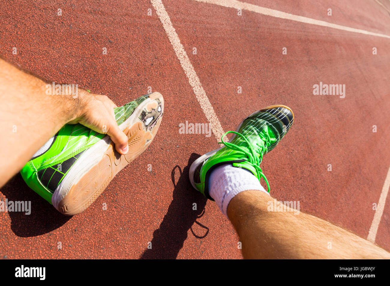 Un atleta esausto su una via di corsa indossando rotto verde scarpe da corsa con grandi fori nella suola. Foto Stock