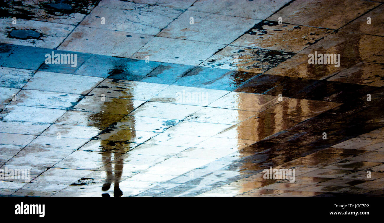 Sfocate ombra di riflessione di una giovane donna che cammina nella vecchia città distrutta zona pedonale subito dopo la pioggia Foto Stock