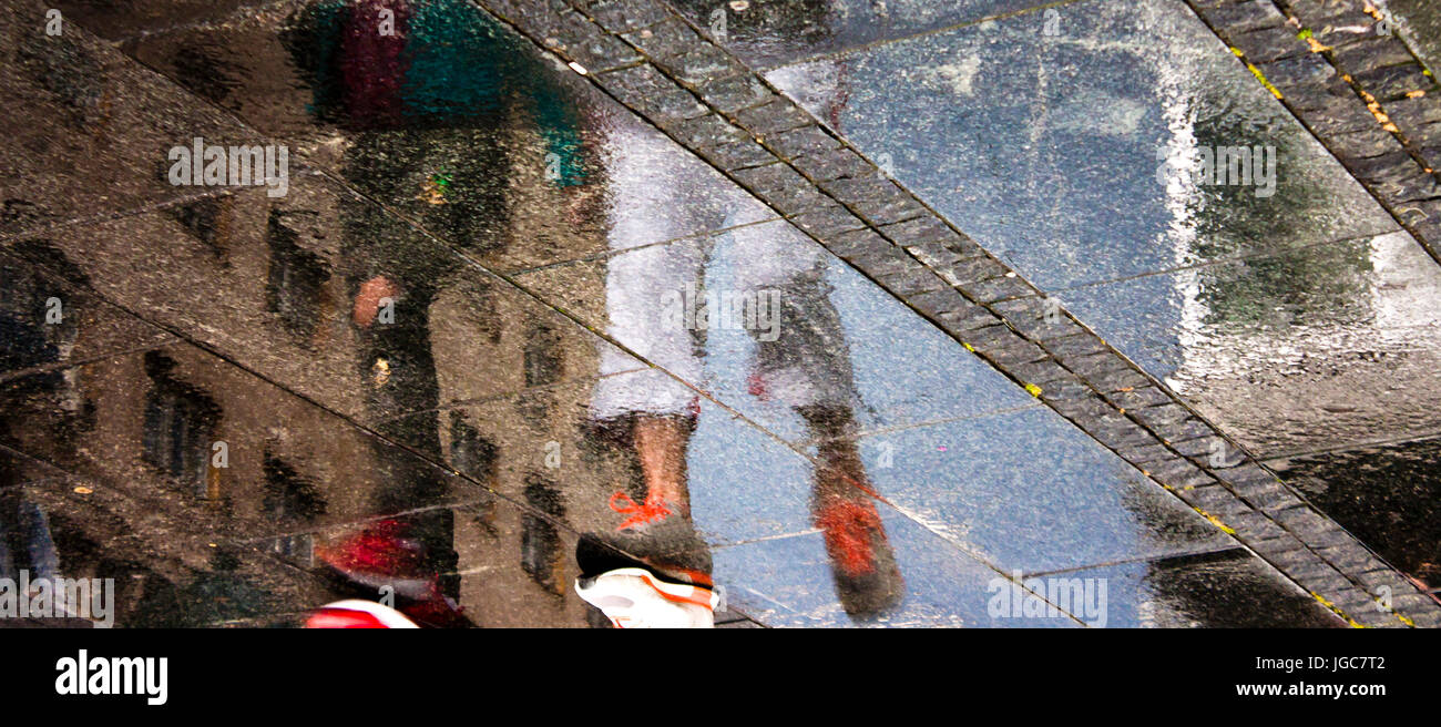 Sfocata la riflessione di due persone a piedi la strada di città in una piovosa giornata d'estate Foto Stock