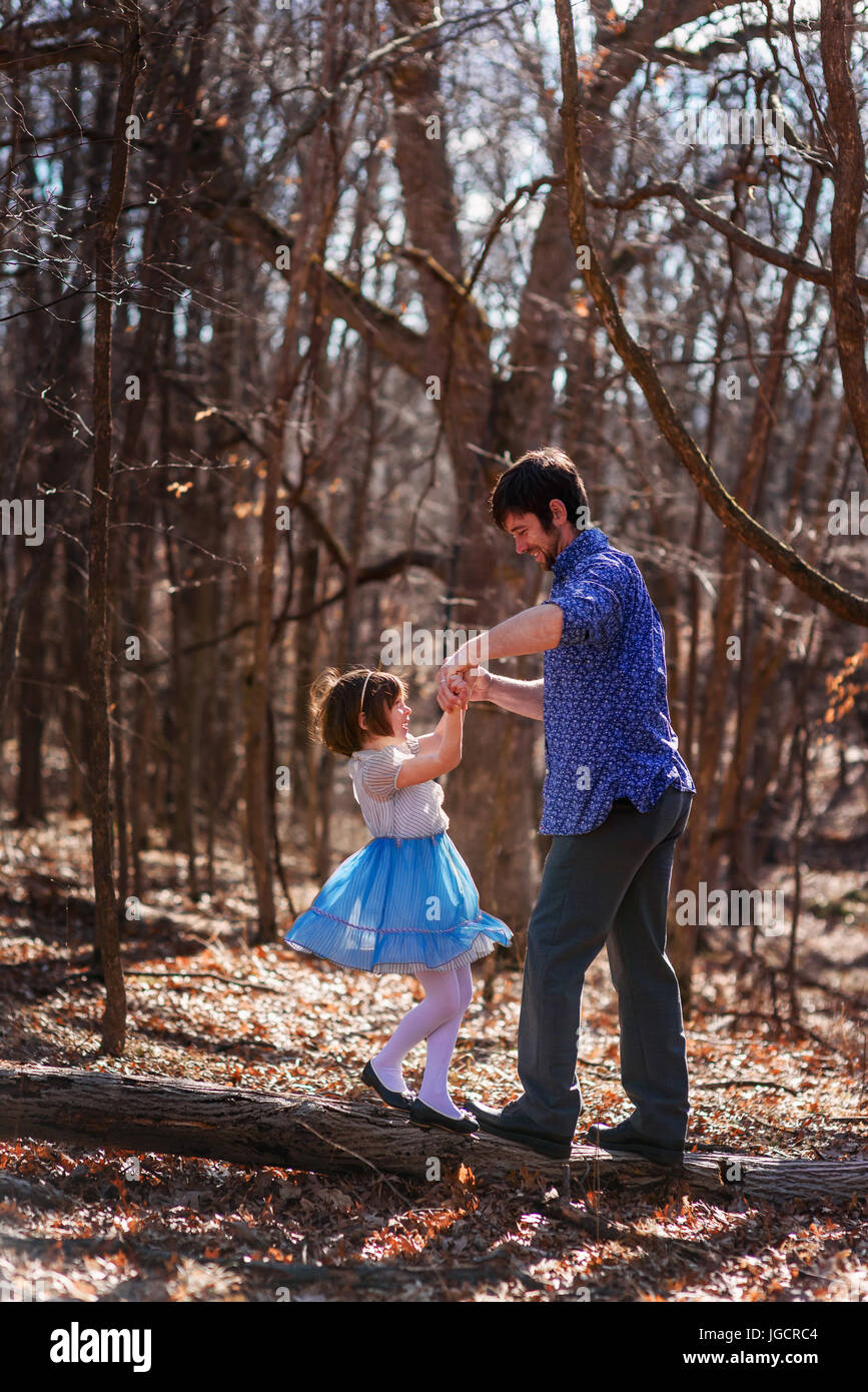 Padre e figlia tenendo le mani in piedi su un tronco di albero nella foresta Foto Stock