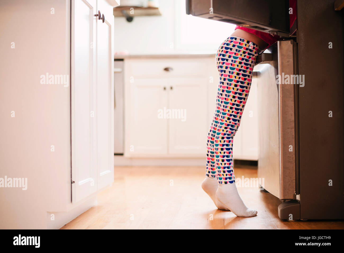 Ragazza alla ricerca di cibo in un frigorifero aperto in cucina Foto Stock