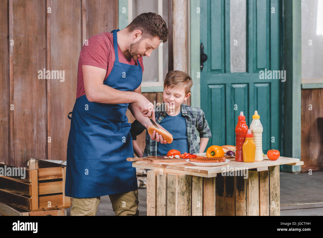 Carino piccolo ragazzo con il padre nel grembiule preparazione di hot dog  insieme nel cortile, papà e figlio concetto di cucina a vista Foto stock -  Alamy