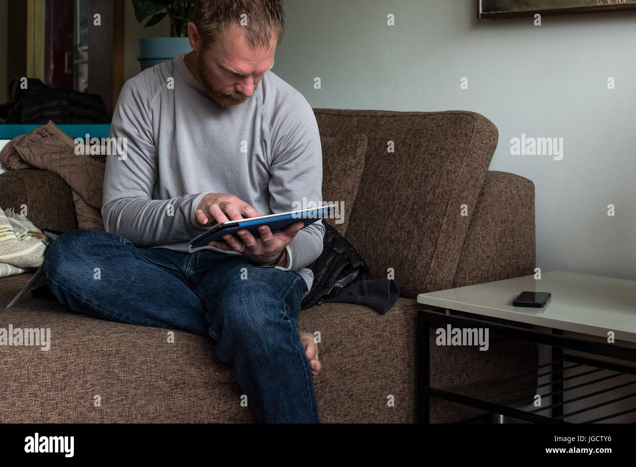 Uomo seduto sul lettino usando una tavoletta digitale Foto Stock