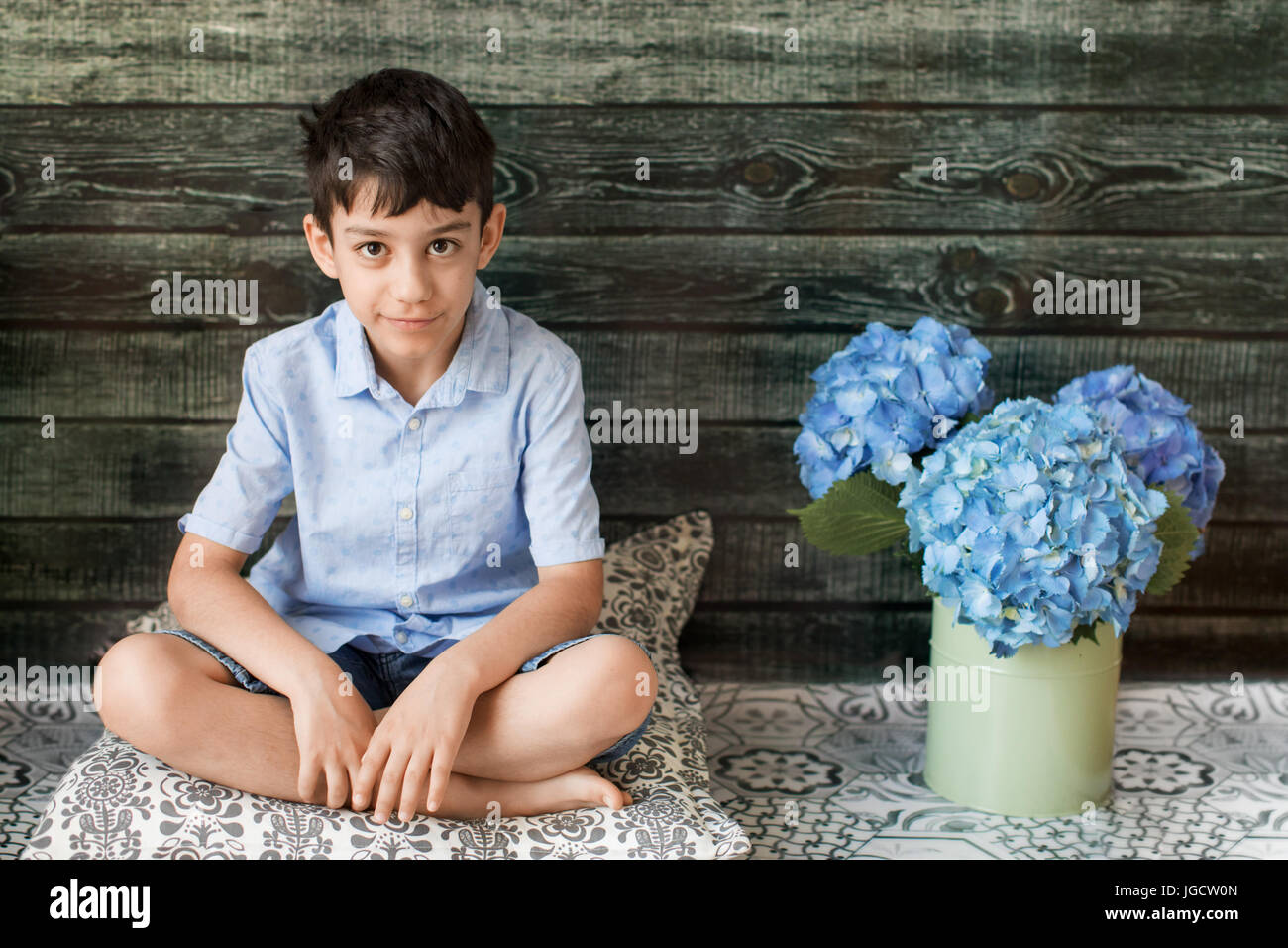 Ragazzo seduto accanto a un vaso con fiori di ortensie Foto Stock