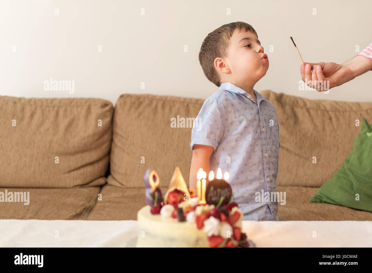 Ragazzo soffiando fuori un match dopo la sua madre ha acceso candele su una torta di compleanno Foto Stock