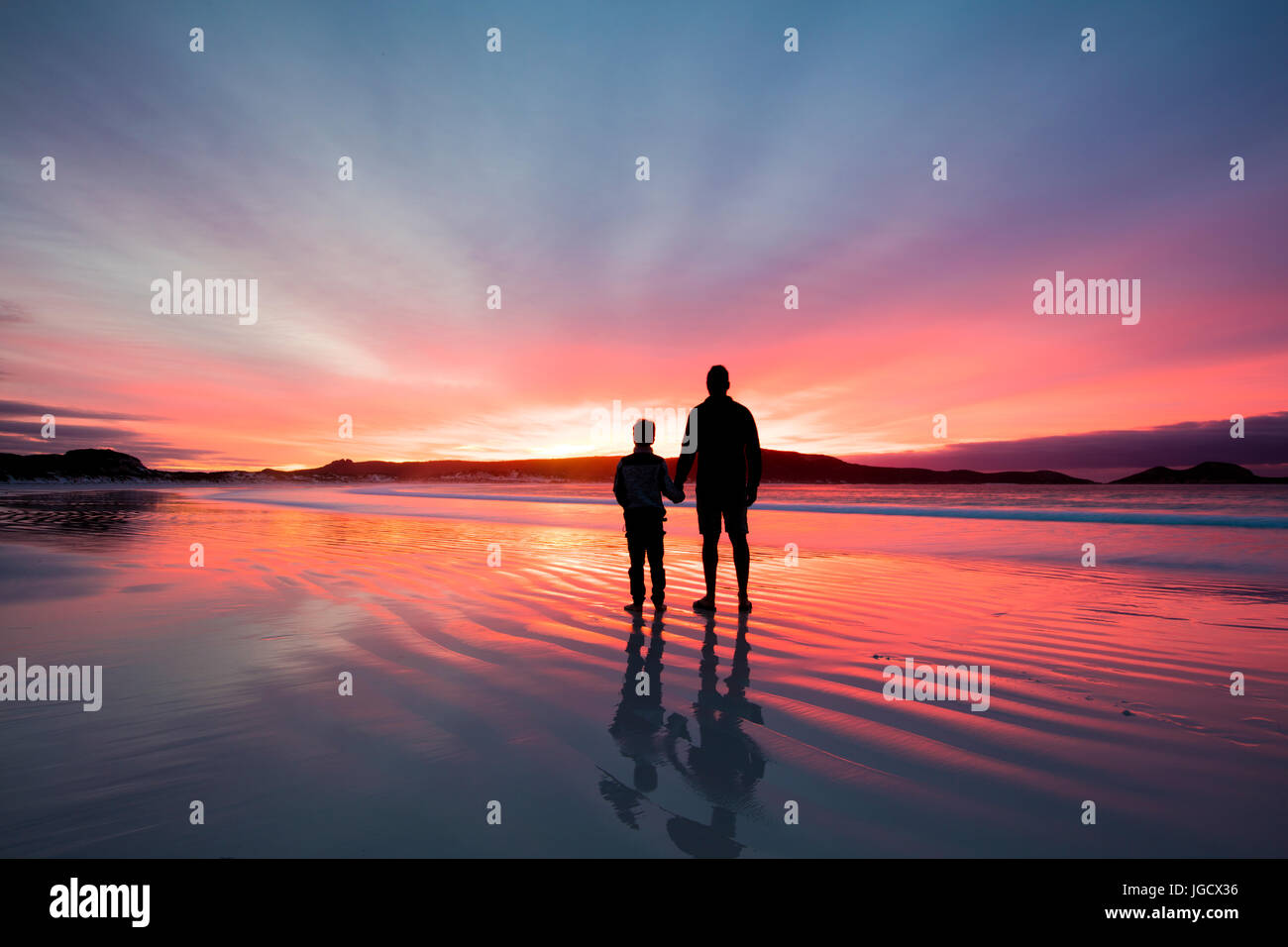 Silhouette di un padre e figlio tenendo le mani sulla spiaggia al tramonto, Australia occidentale, Australia Foto Stock