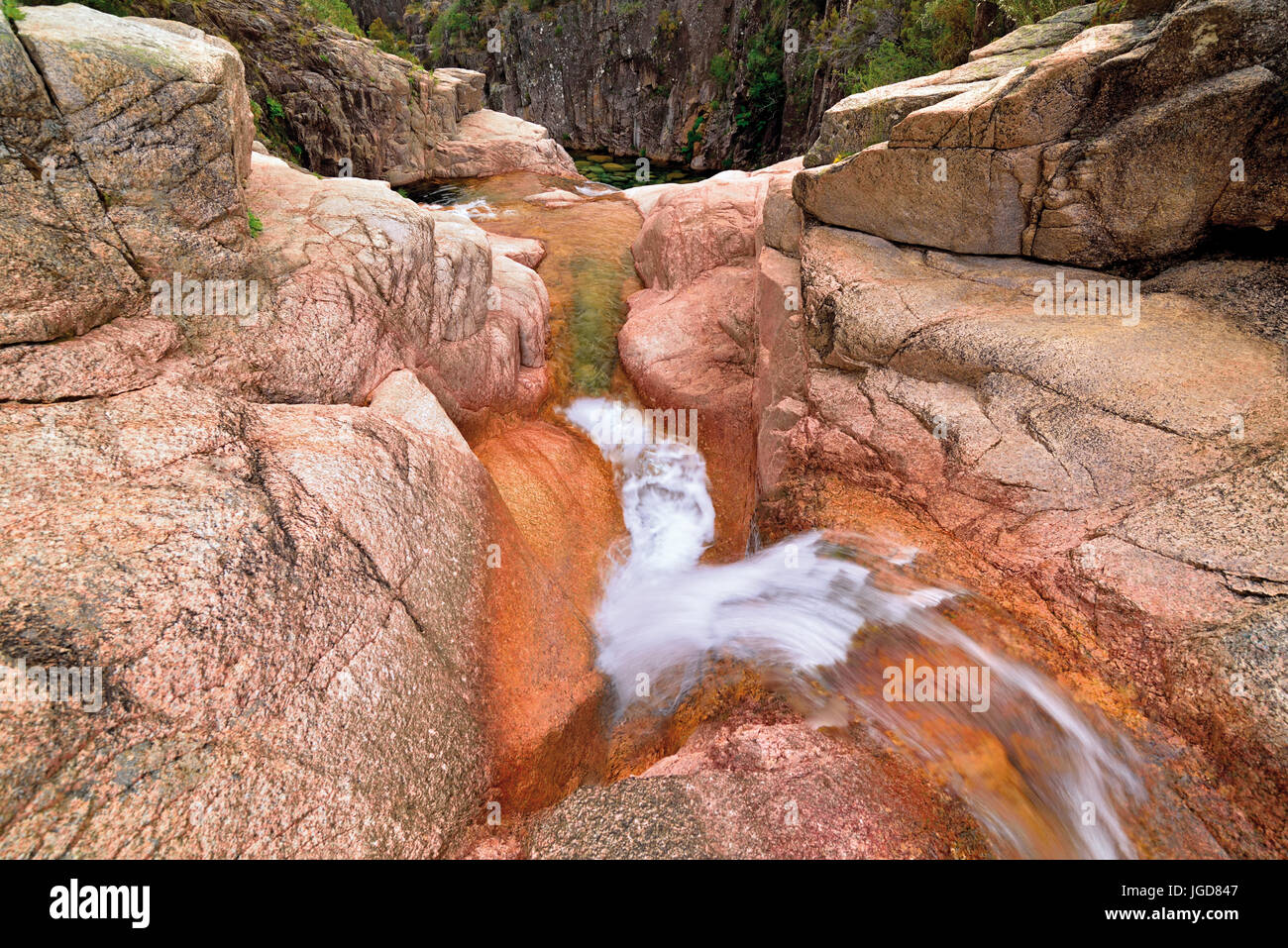 Una piccola cascata nel burrone di montagna con enormi rocce Foto Stock