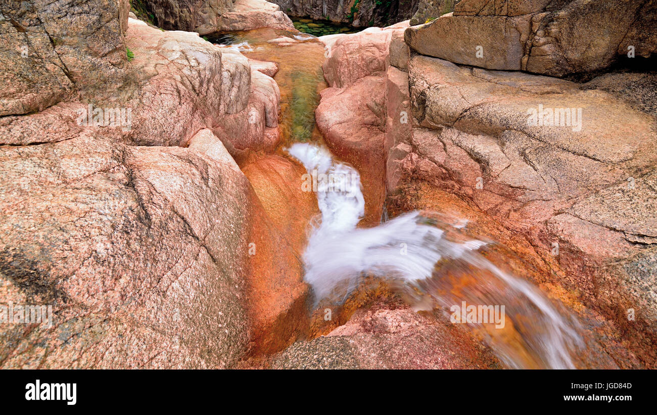 Una piccola cascata nel burrone di montagna con enormi rocce Foto Stock