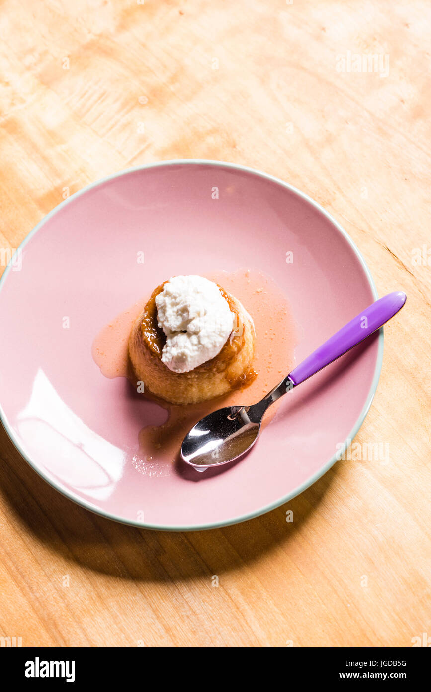 Flan - un dolce crema pasticcera creme caramel con crema sulla parte superiore, su una piastra di rosa su una tavola di legno. Foto Stock