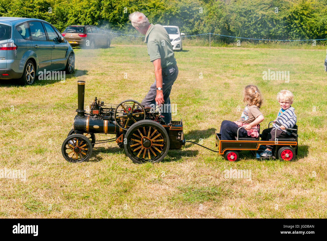 L uomo alla guida della sua replica in miniatura Modello in scala i motori di trazione con i suoi due bambini in un rimorchio a un rally a vapore Foto Stock