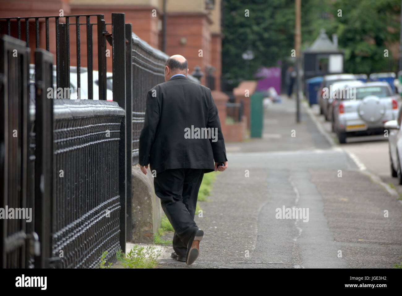 Imprenditore sovrappeso ben vestito maschile in una tuta da dietro sulla strada a circa per entrare nell'edificio con ringhiere in nero Foto Stock