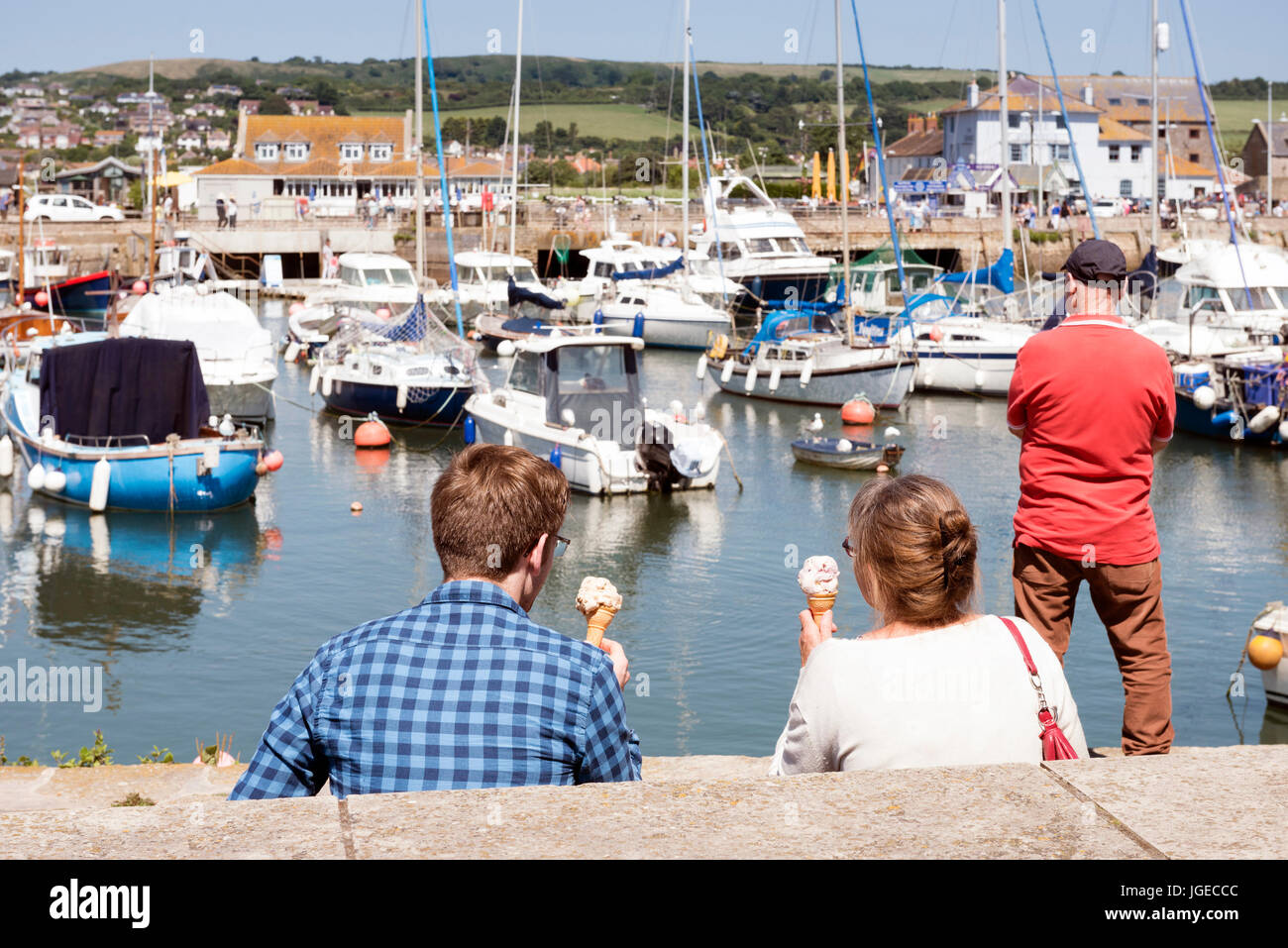 Persone mangiare gelati e si affaccia sul porto di West Bay, Dorset, Regno Unito. Foto Stock