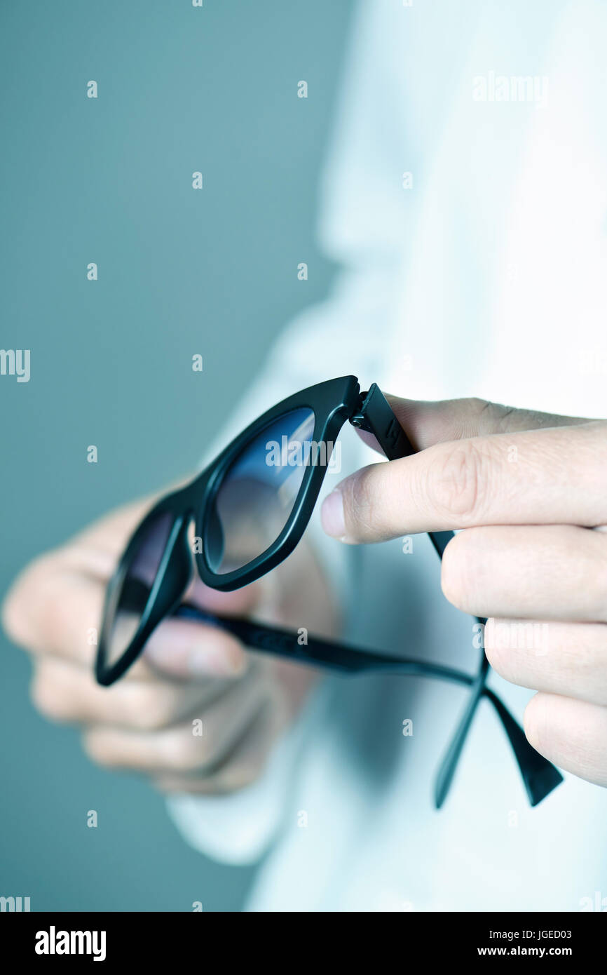 Primo piano di un giovane uomo oculista in camice bianco con un paio di occhiali da sole nelle sue mani Foto Stock