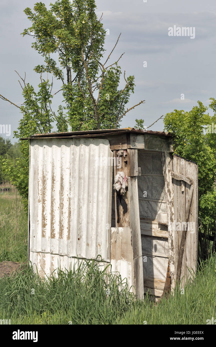 Vecchia fatiscente in legno wc campeggio in un villaggio tra gli alberi e gli arbusti. Foto Stock