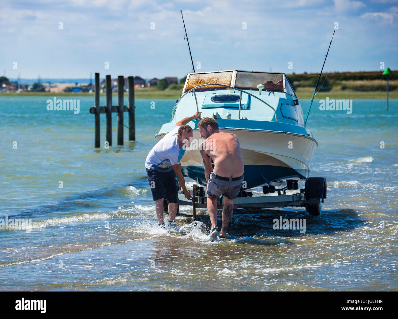 Due uomini tirando una piccola imbarcazione a motore al di fuori del mare lungo una sorta di scivolo. Foto Stock
