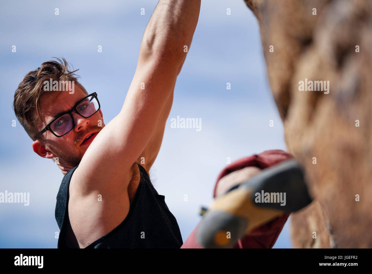 Montare giovane uomo caucasico con gli occhiali rock si arrampica nel deserto Foto Stock