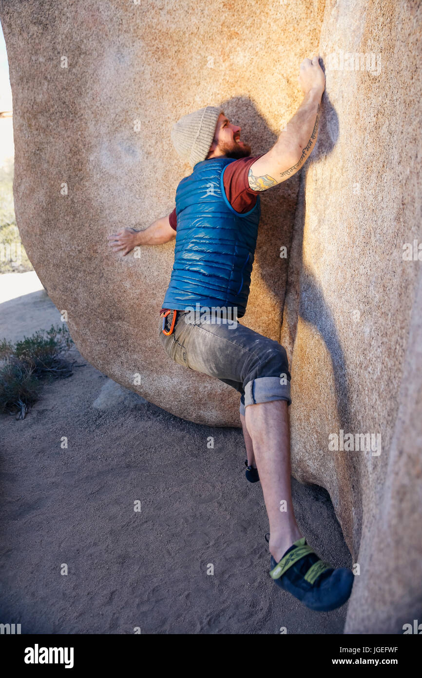 Giovane uomo caucasico con barba salite di roccia nel deserto con nessuna attrezzatura di sicurezza Foto Stock