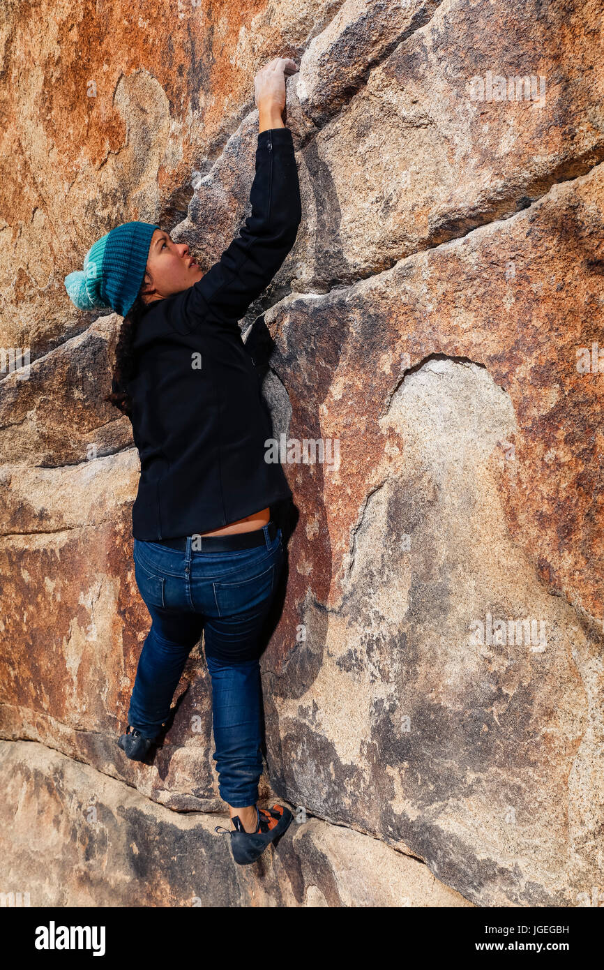 Giovani razza mista donna si arrampica su una parete di roccia nel deserto Foto Stock