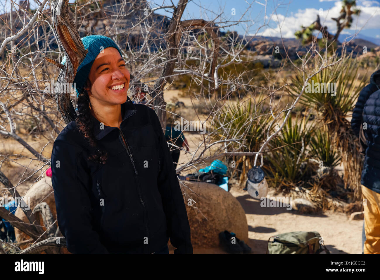 Giovani razza mista donna sorrisi e rilassa mentre si guarda amici arrampicata nel deserto Foto Stock
