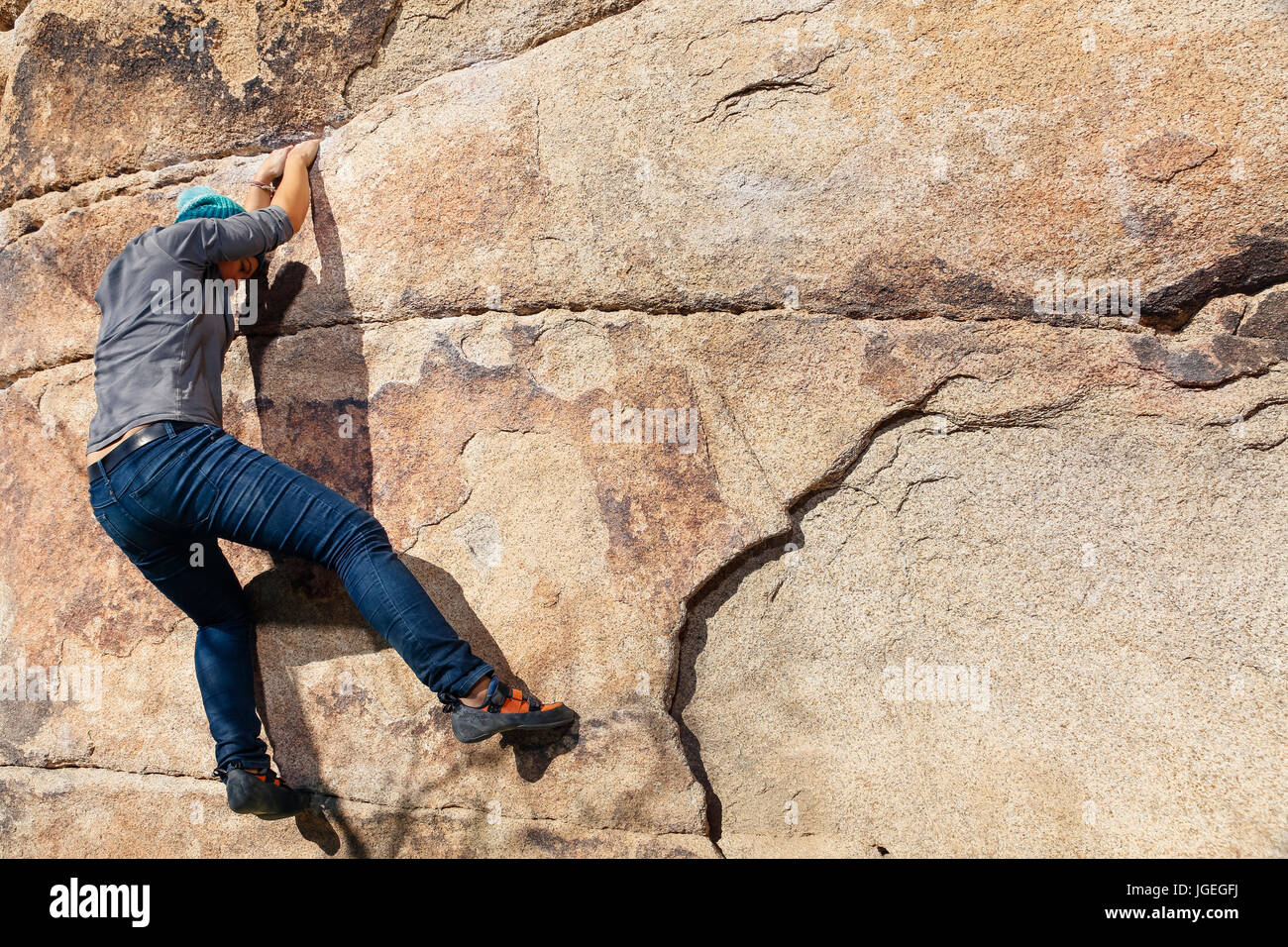 Giovani razza mista donna si arrampica su una parete di roccia nel deserto Foto Stock