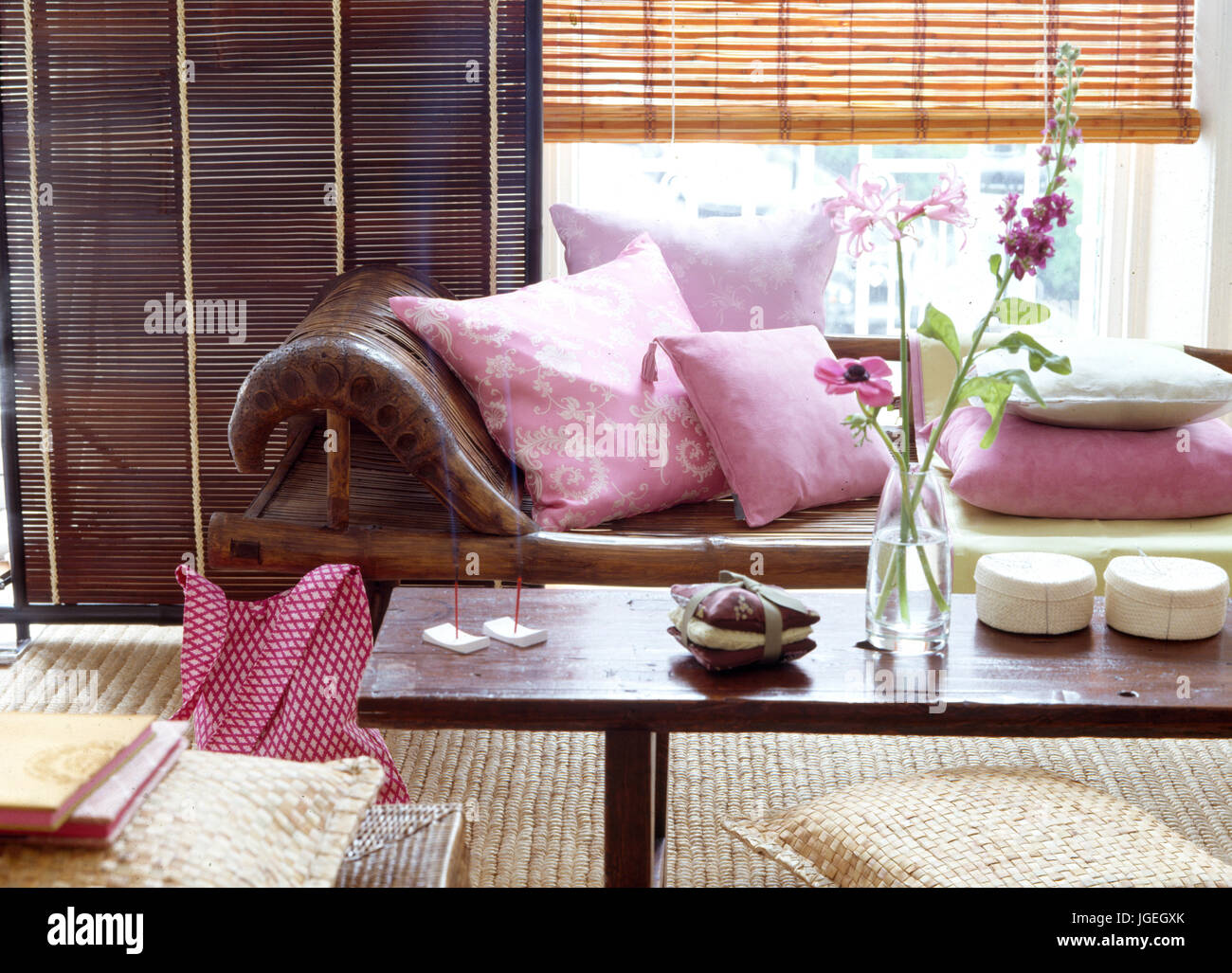 Pelle marrone con chaise longue con cuscini di colore rosa di fronte a finestre ith split-persiane di canna Foto Stock