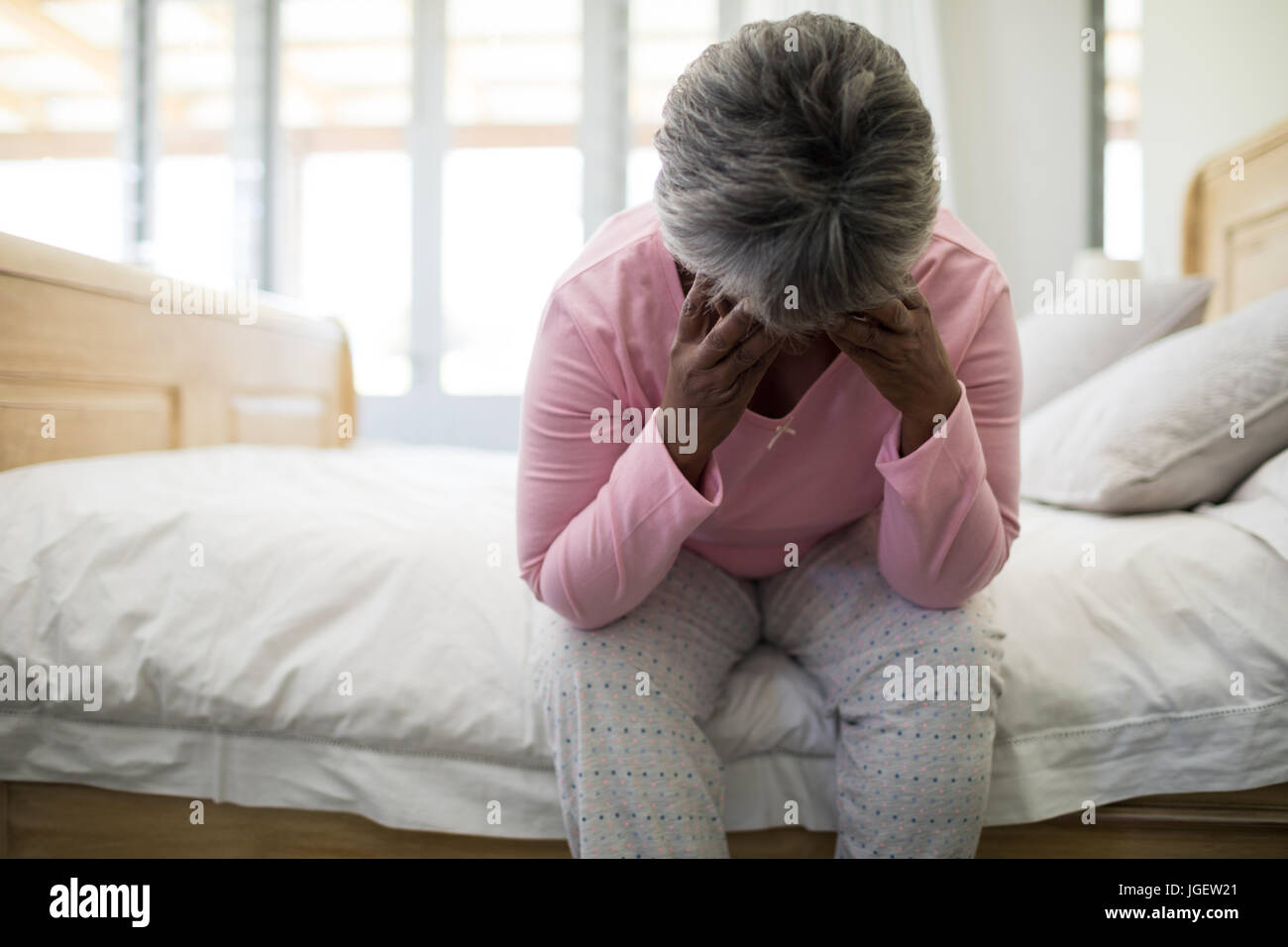 Tense senior donna seduta sul letto in camera da letto a casa Foto Stock