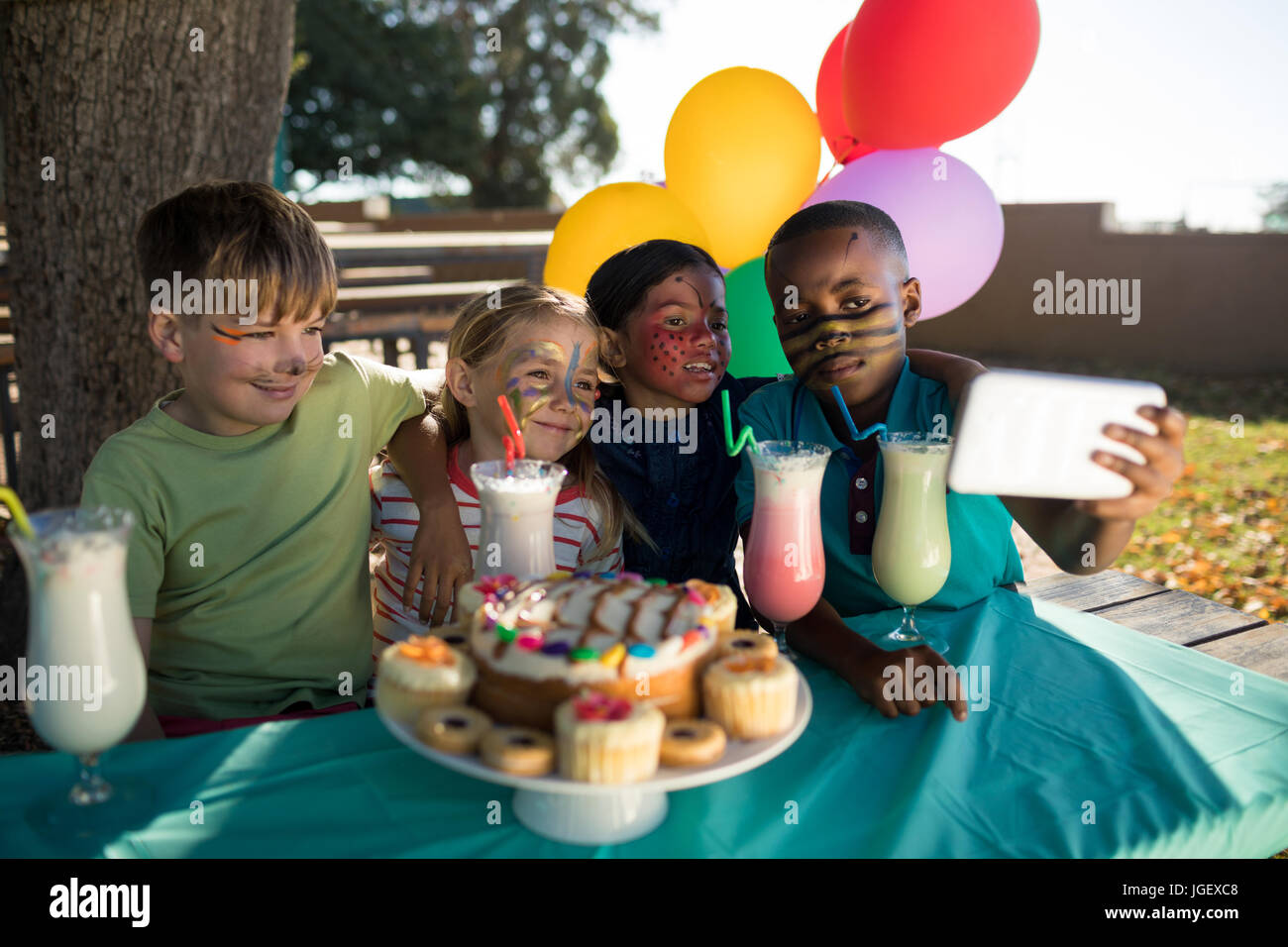 Ragazzo tenendo selfie con gli amici mentre è seduto da cibi e bevande presso il park Foto Stock