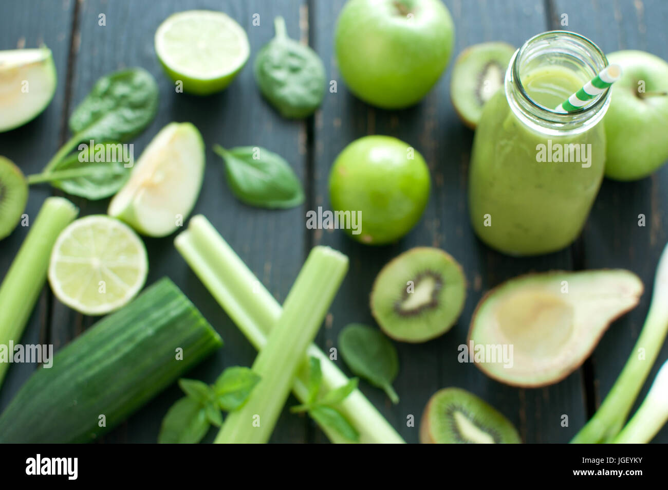 Gli ingredienti freschi intorno a un frullato verde bottiglia con paglia Foto Stock