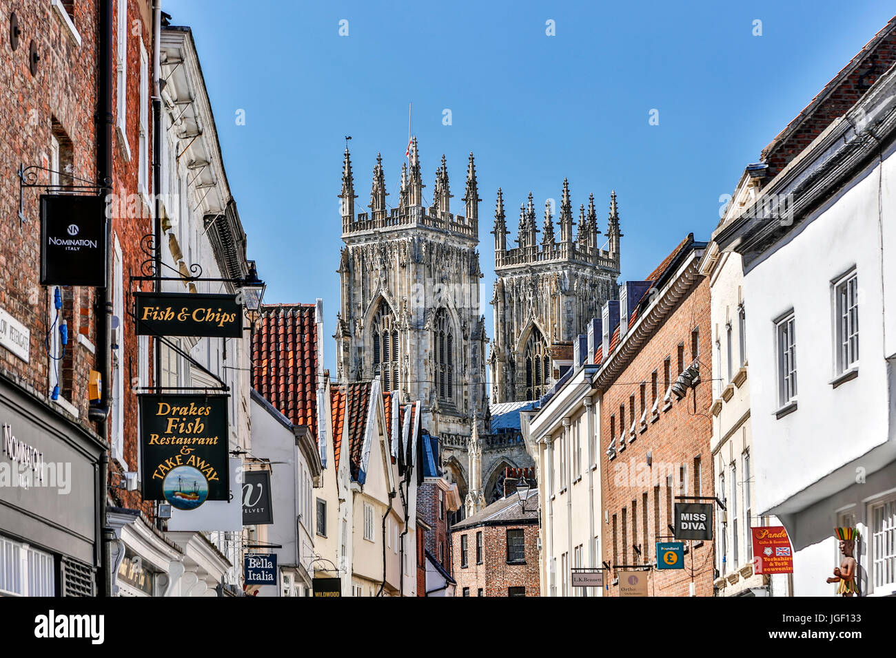 Negozi, segni e le torri della cattedrale di York Minster (la Cattedrale Metropolitical e Chiesa di San Pietro in background, York, nello Yorkshire, Inghilterra, Regno Unito Foto Stock