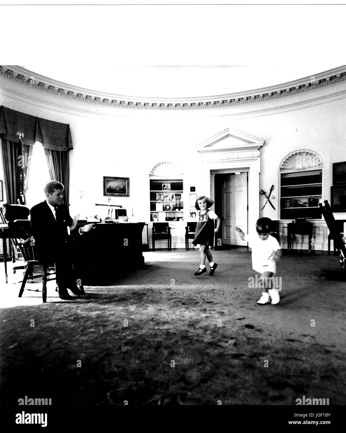 Il presidente statunitense John F Kennedy lavora nell'Ufficio Ovale della Casa Bianca mentre i bambini John Kennedy Jr e Caroline Kennedy play, Ottobre 10, 1962. Foto di Cecil Stoughton. Foto Stock