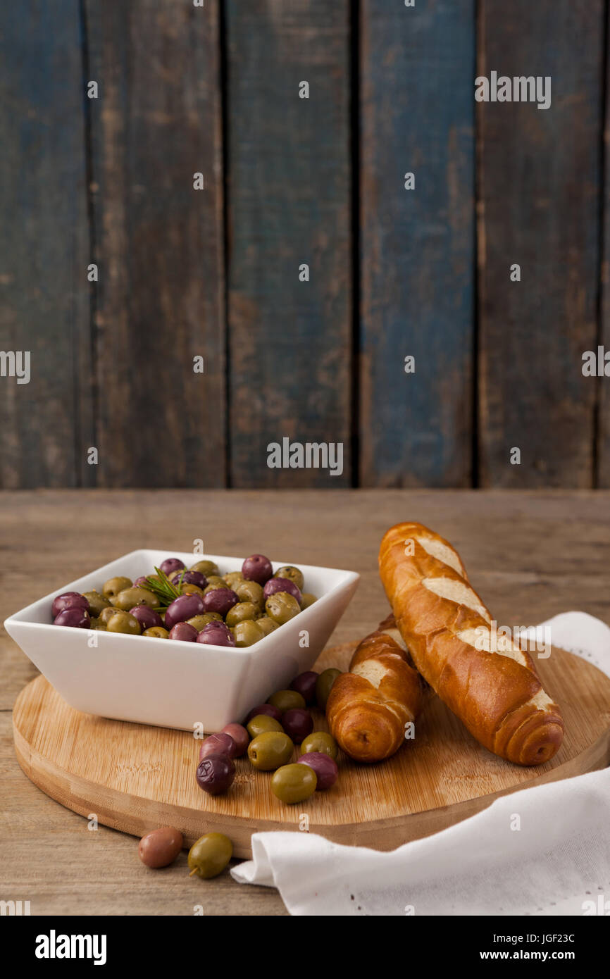 Le olive nel contenitore da pane sul tagliere al tavolo contro la parete Foto Stock