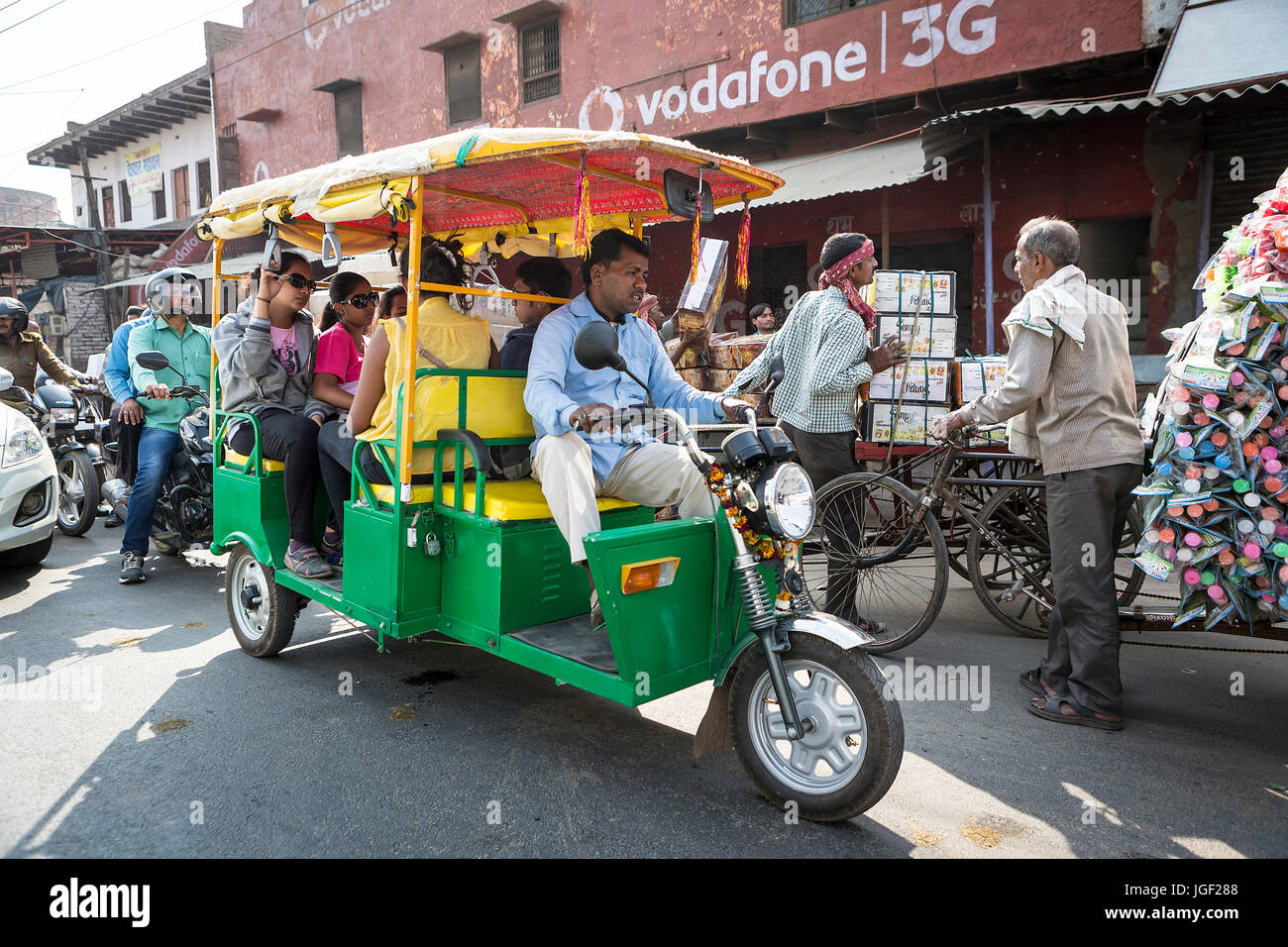 Il giallo e il verde a tre ruote taxi capi di una strada trafficata in India Foto Stock