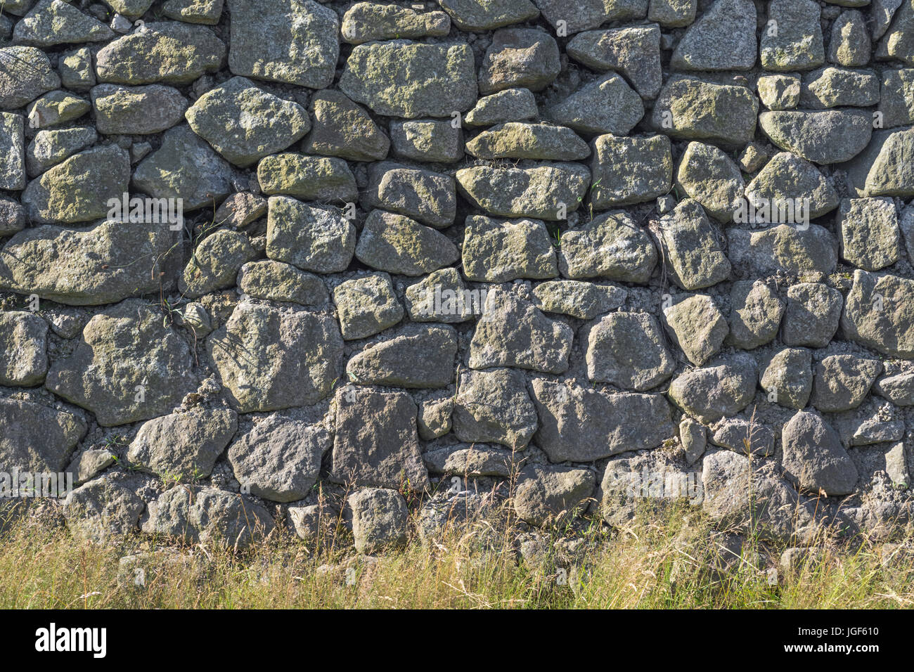 Pietra irregolare / parete di granito a lato della strada con erba verga vegetazione. Foto Stock