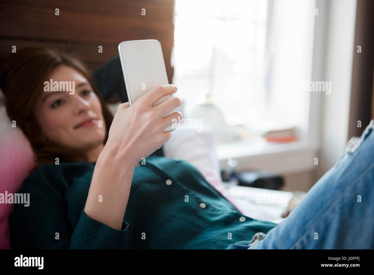 La donna caucasica posa nel letto i messaggi di testo sul telefono cellulare Foto Stock