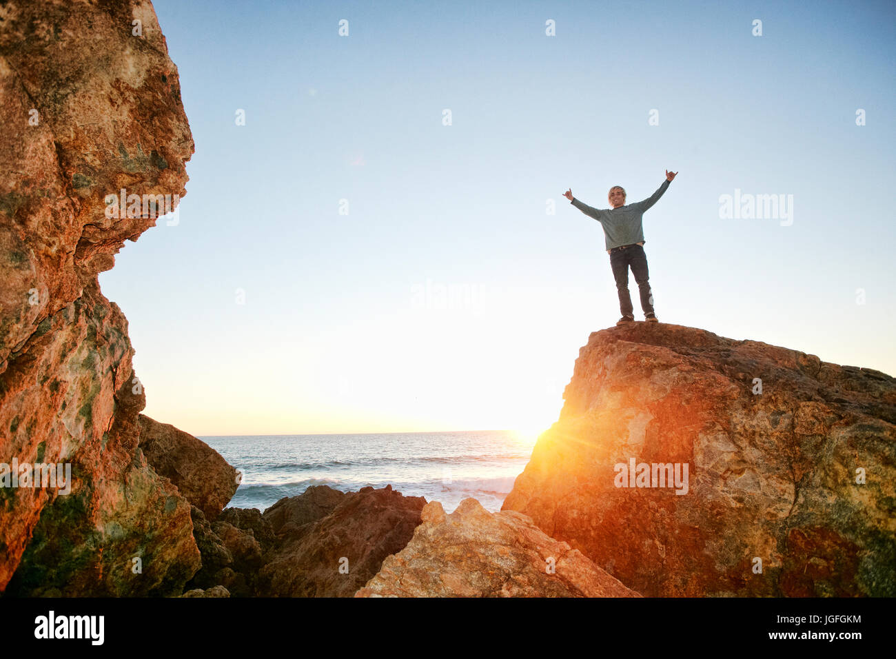 Uomo caucasico in piedi con le braccia alzate su roccia a ocean Foto Stock