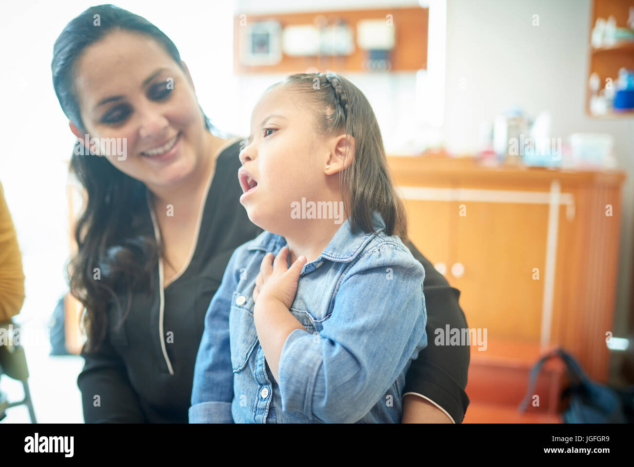 Madre ispanica guarda la figlia con la sindrome di Down che puntano a collo Foto Stock