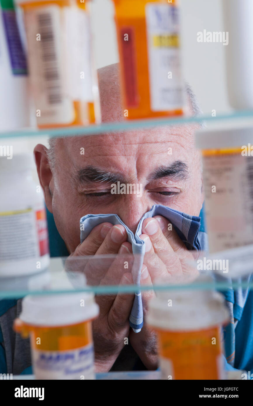 Uomo ispanico tergi naso vicino Armadietto dei medicinali Foto Stock