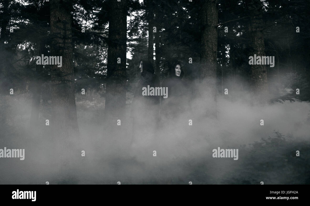 La gente che indossa abiti neri e maschere bianche nella foresta di nebbia Foto Stock
