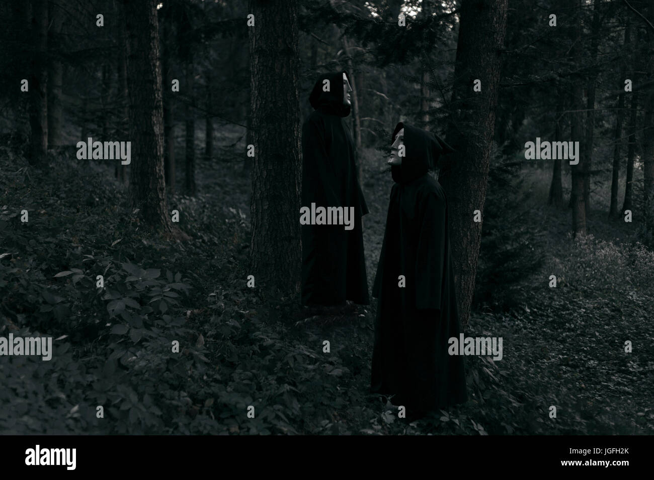 La gente che indossa abiti neri e maschere bianche in piedi nella foresta Foto Stock
