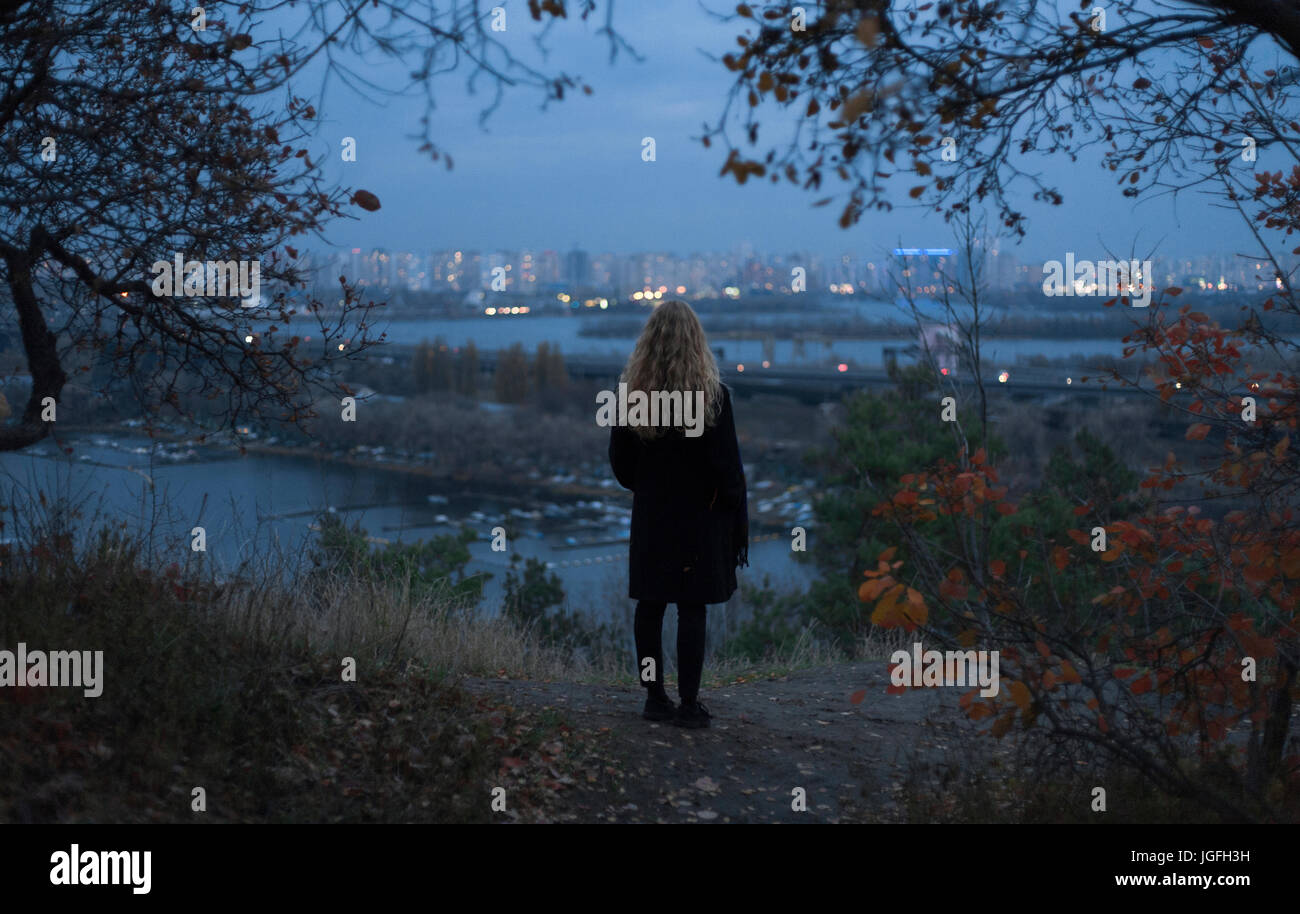 Malinconici Caucasian donna in piedi vicino a waterfront urbano di notte Foto Stock